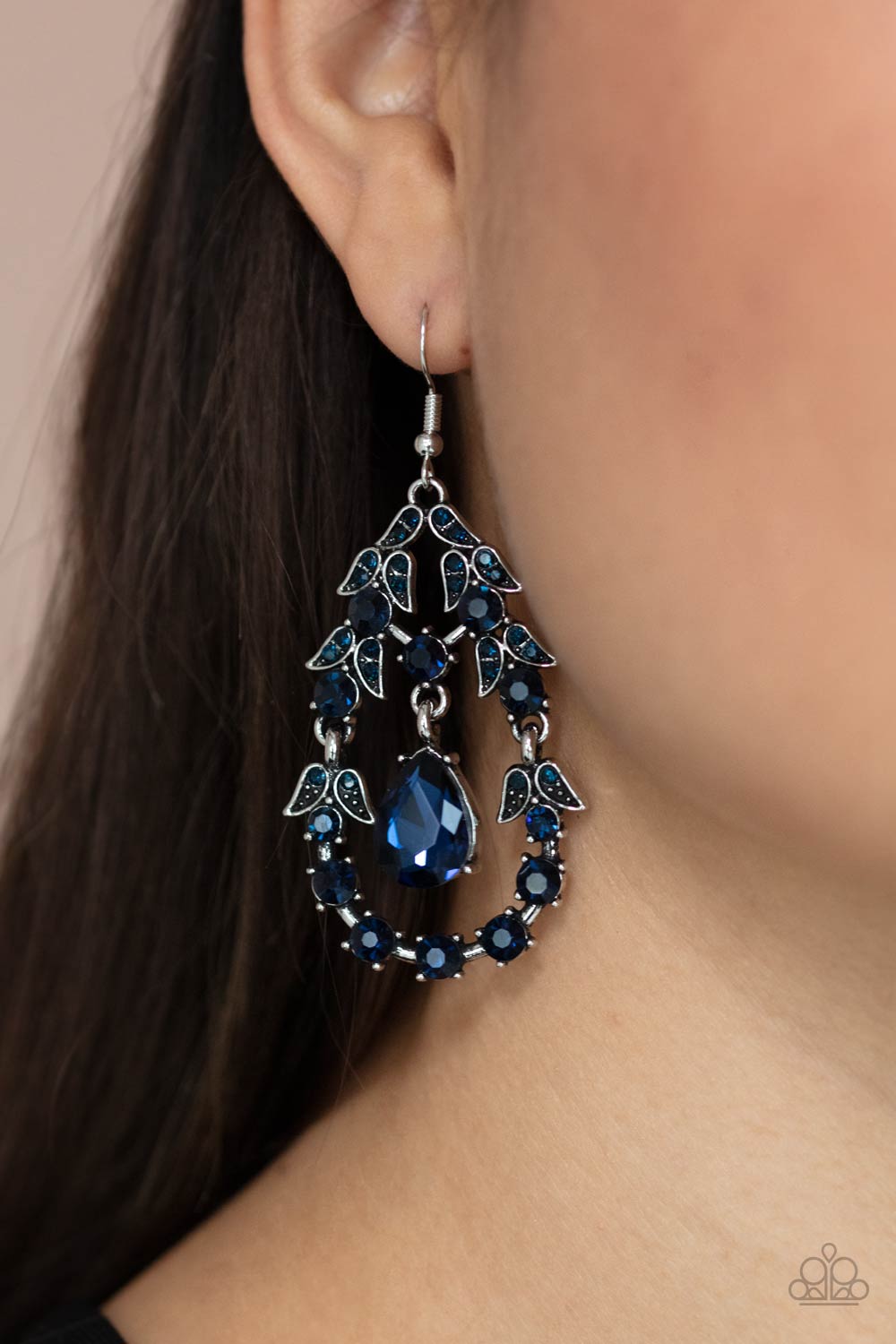 A solitaire blue teardrop rhinestone swings from the top of an ornately hinged teardrop frame adorned in blue rhinestone dotted leafy silver frames, creating a glamorous centerpiece. Earring attaches to a standard fishhook fitting. Sold as one pair of earrings.&amp;nbsp;